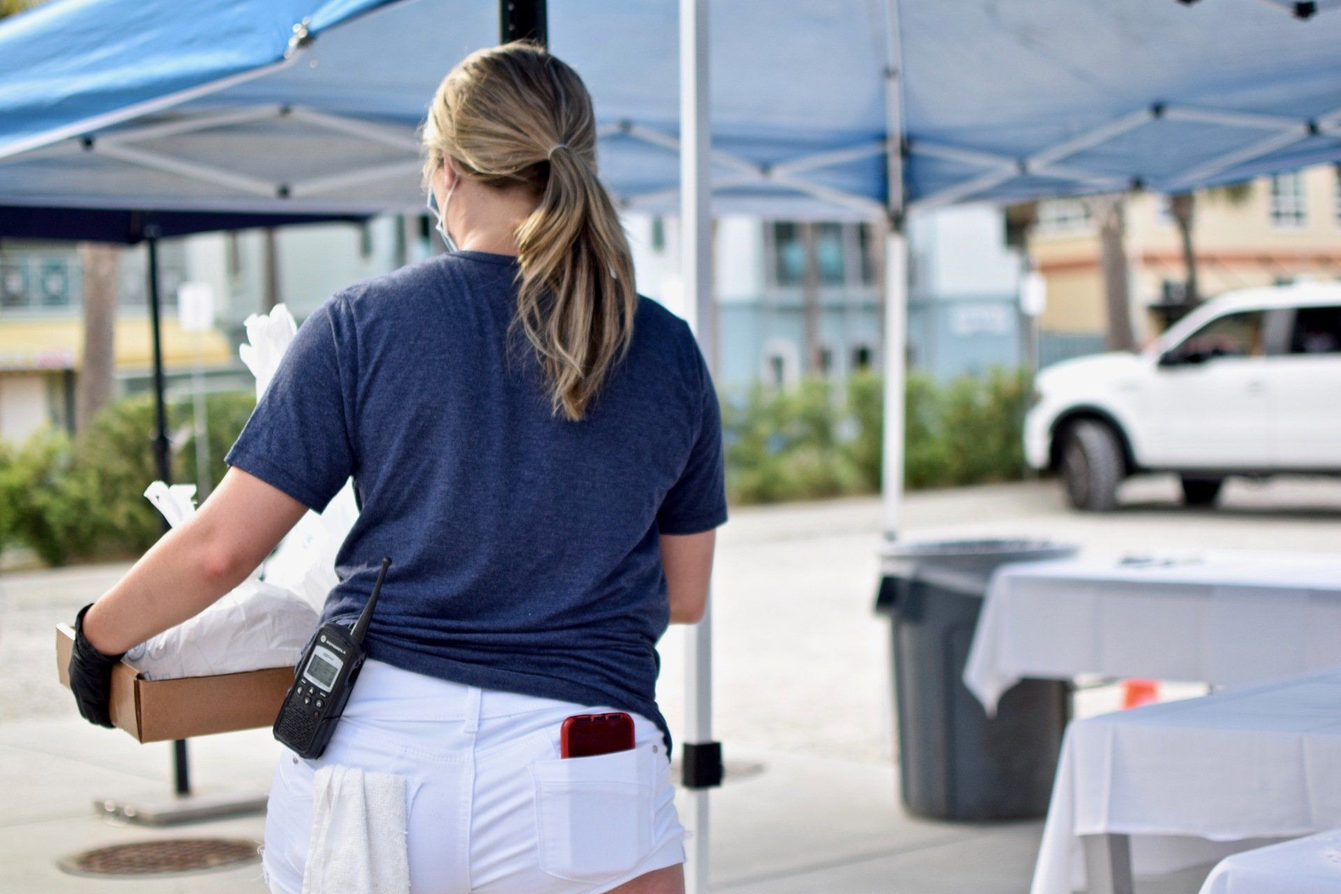 Volunteer carrying a box under blue tents at an outdoor event