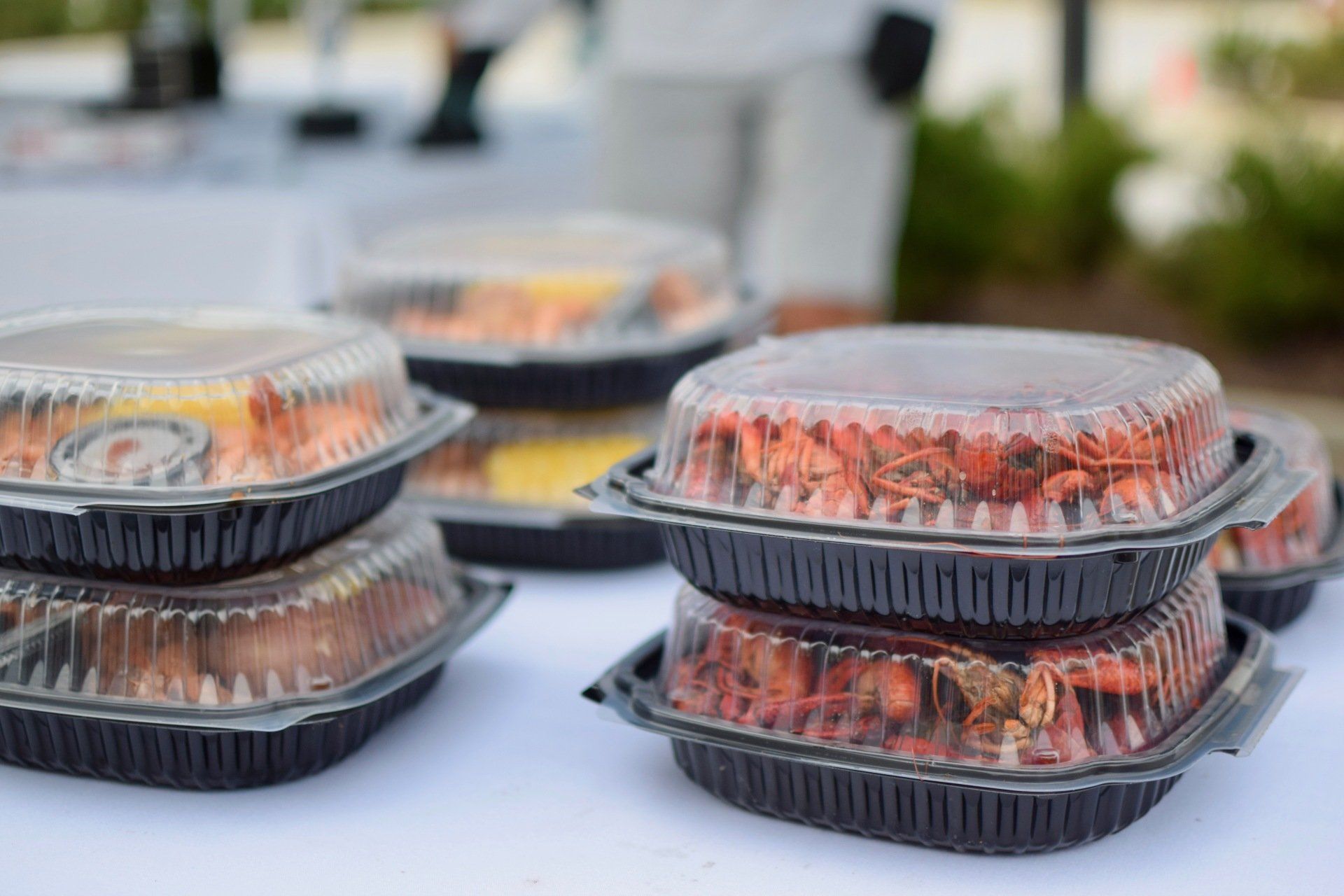Stacked plastic takeout containers with grilled food on a table outdoors