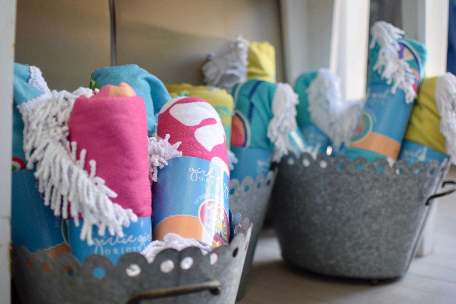 Colorful folded blankets in gray baskets on a shelf, with tassels and patterned fabric visible.
