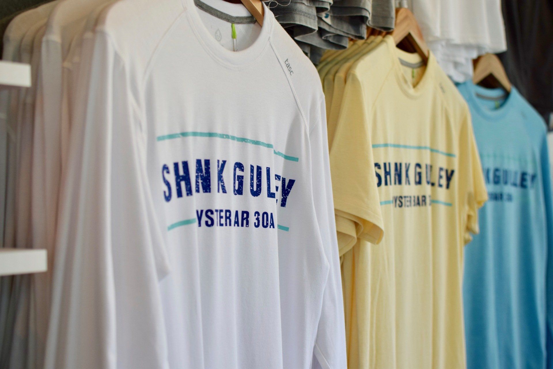 Hanging SHANG-GUY Yeshar 30 T-shirts in white, yellow, and blue on clothing racks
