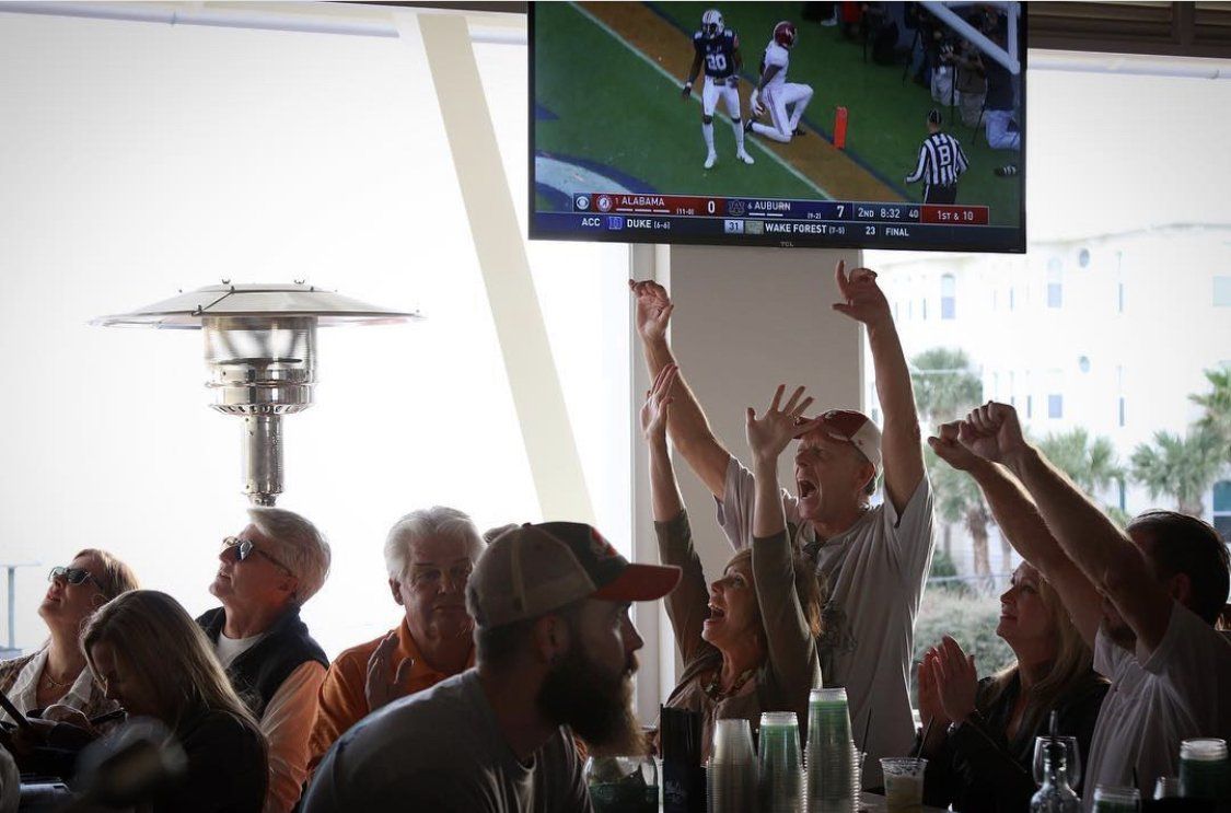 Crowd cheering in a bar while watching a sports game on TV above the room