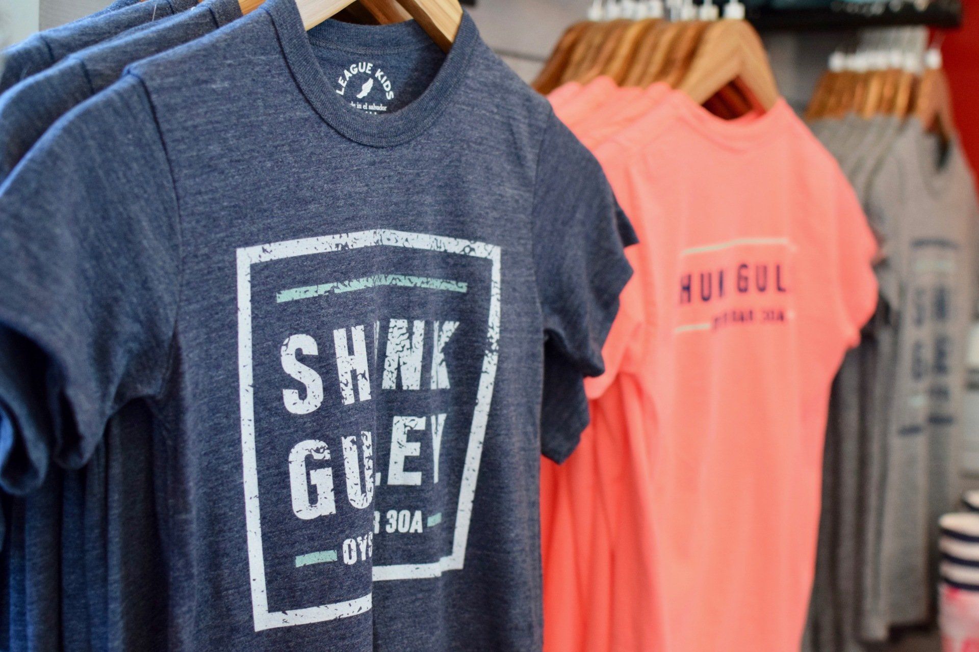 Graphic T-shirts hanging on a clothing rack, including navy and coral shirts with bold prints