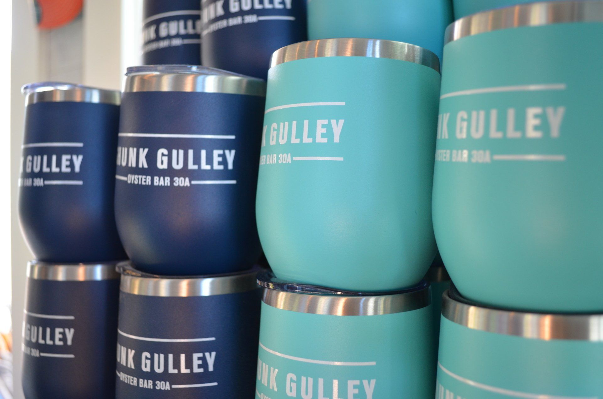 Turquoise and navy Gulley-branded stainless steel tumblers stacked on a shelf