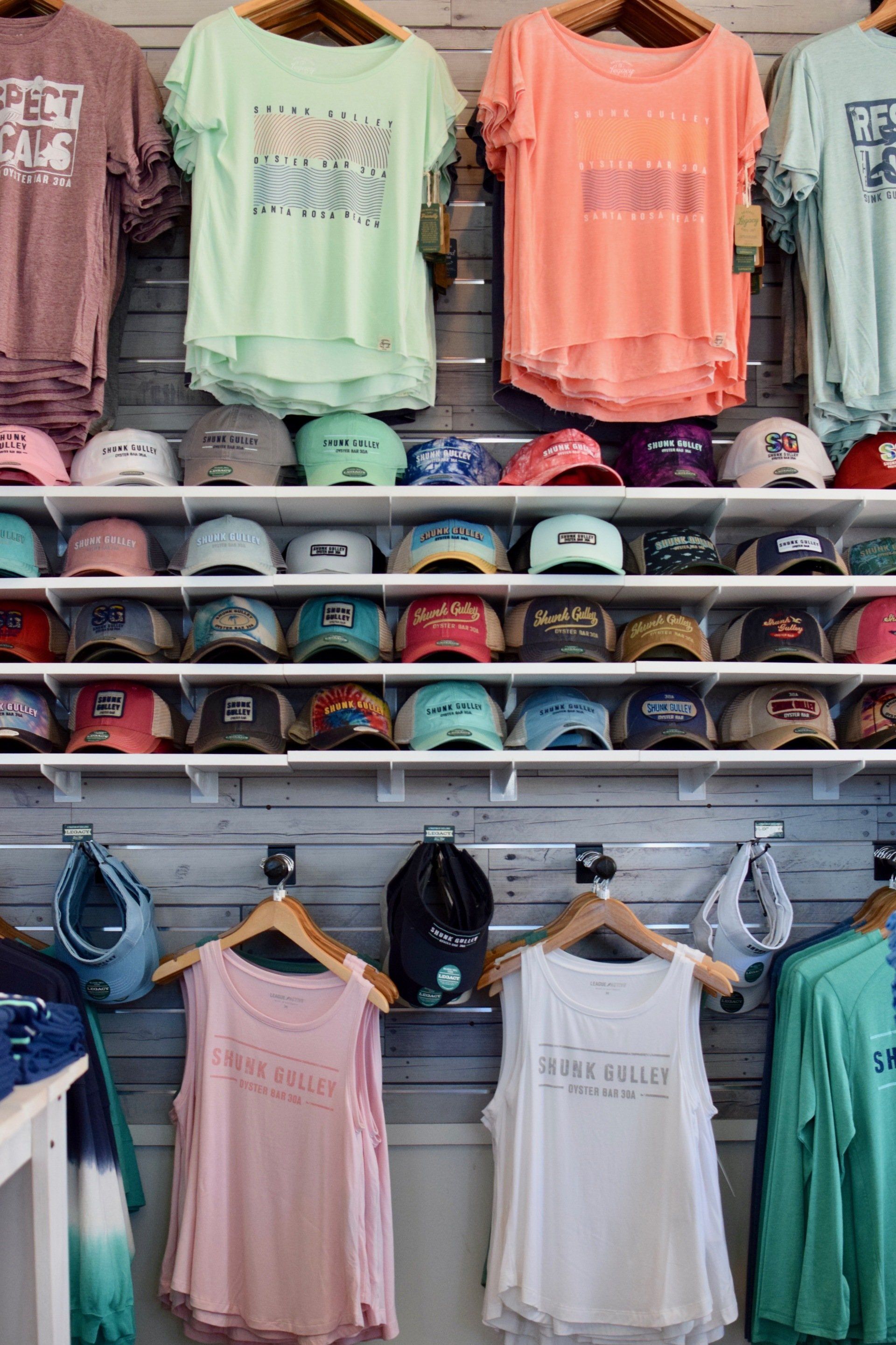 Retail display of pastel graphic T-shirts, baseball caps, and tank tops on store shelves and hangers