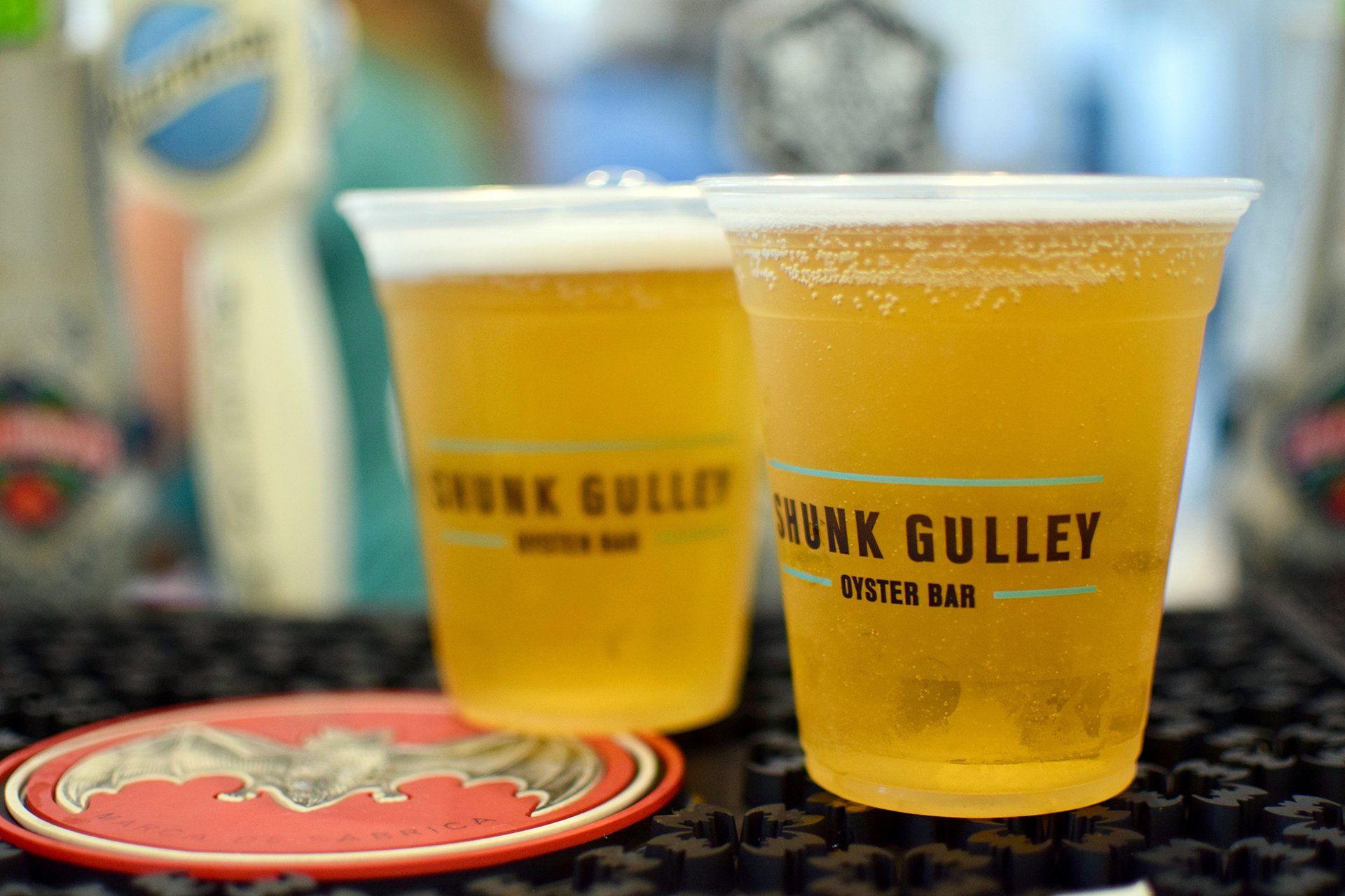 Two plastic cups of amber beer on a bar mat, with a red coaster in the foreground.