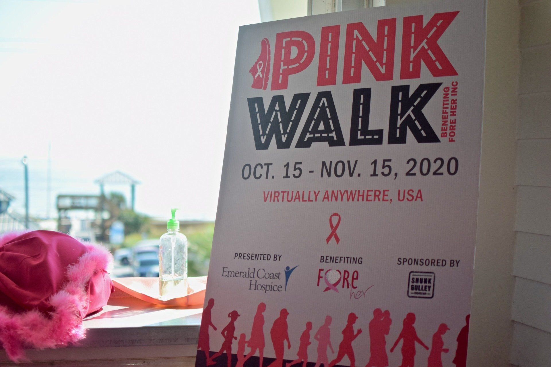 Pink Walk event poster with dates, ribbon logo, and a tabletop display beside it