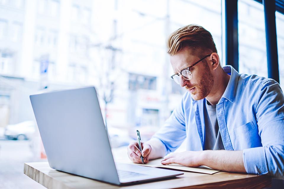 man taking down notes from laptop