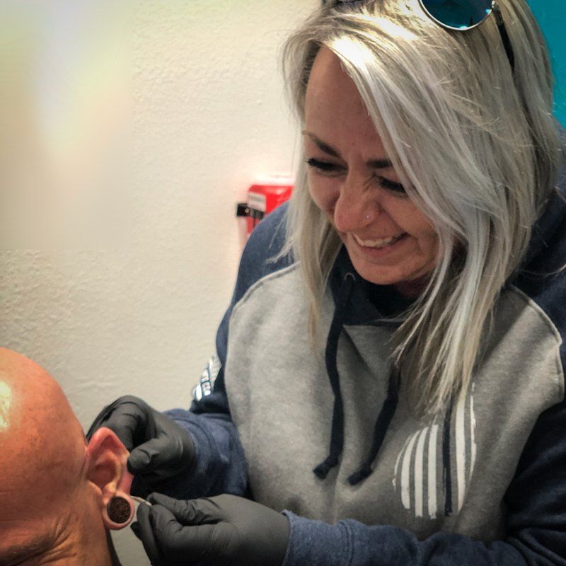 A woman is piercing a man 's ear and smiling