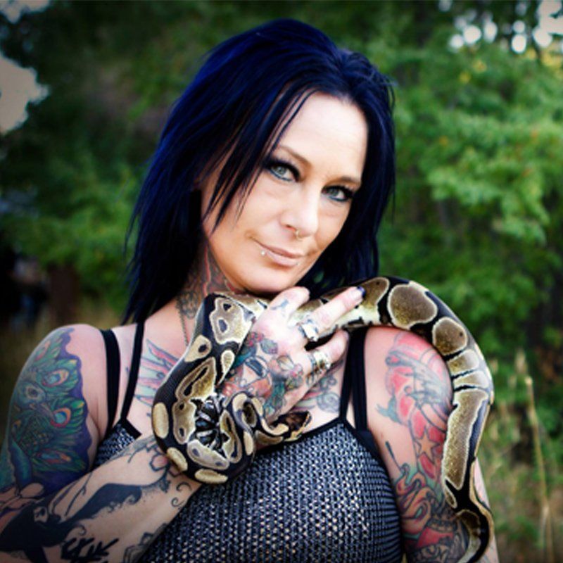 A woman with blue hair is holding a snake on her arm