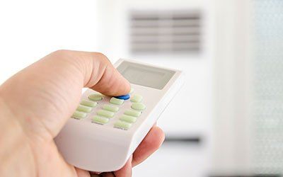 Hand with remote control directed on the conditioner - HVAC Contractors in Lebanon, MO Hand with remote control directed on the conditioner - HVAC Contractors in Lebanon, MO