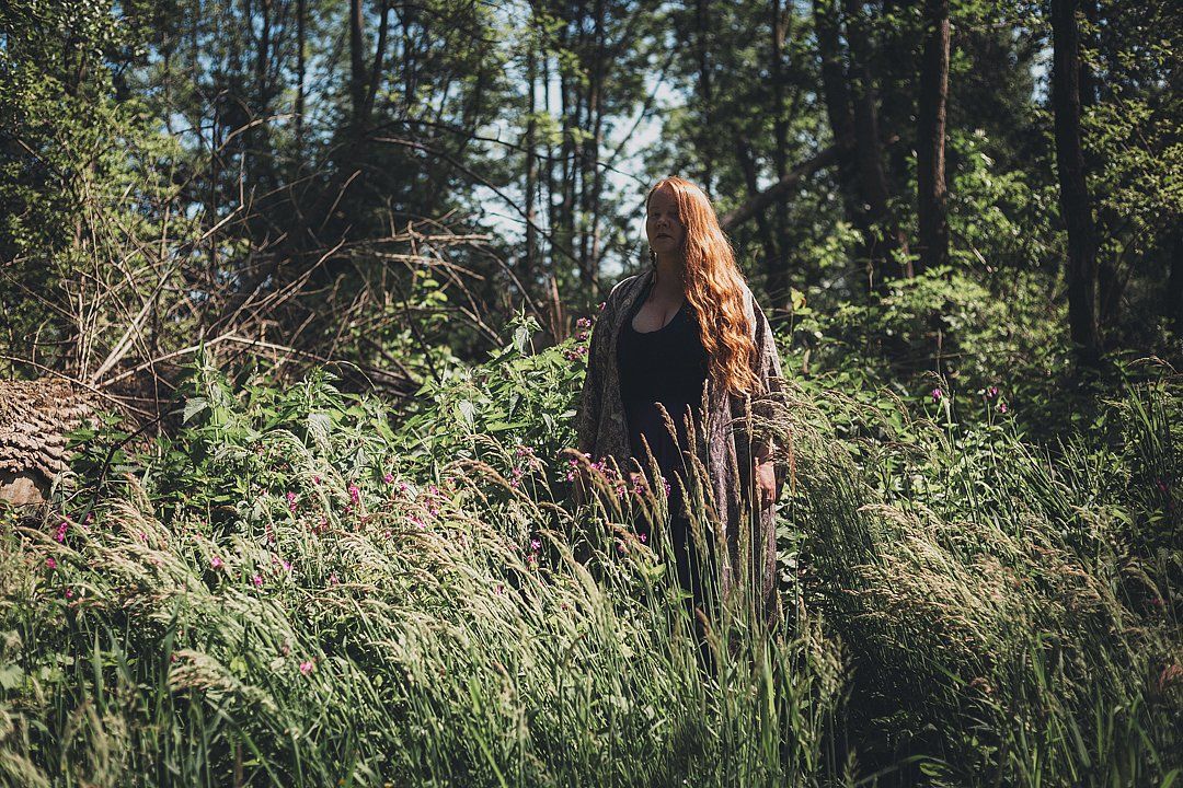 Layla Zoe with her long, red locks of hair standing in a forest setting.