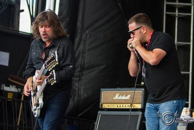 Paul Deslauriers au cheveux longs jouant sa guitare avec un harmoniciste