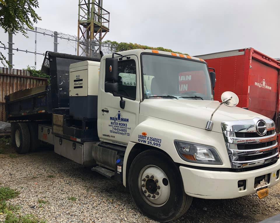 A white dump truck is parked in a gravel lot next to a red truck.