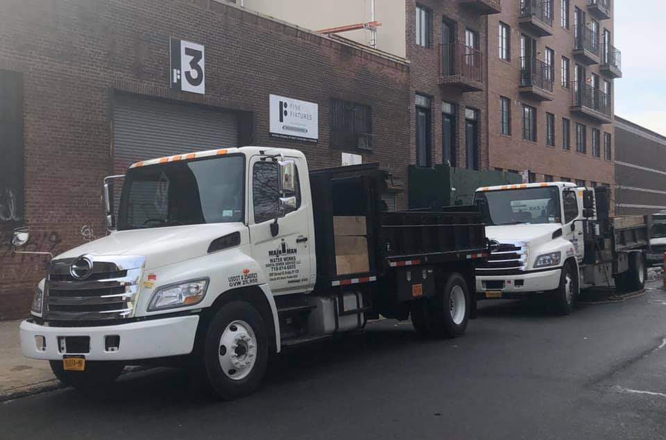Two dump trucks are parked in front of a building with the number 3 on it.