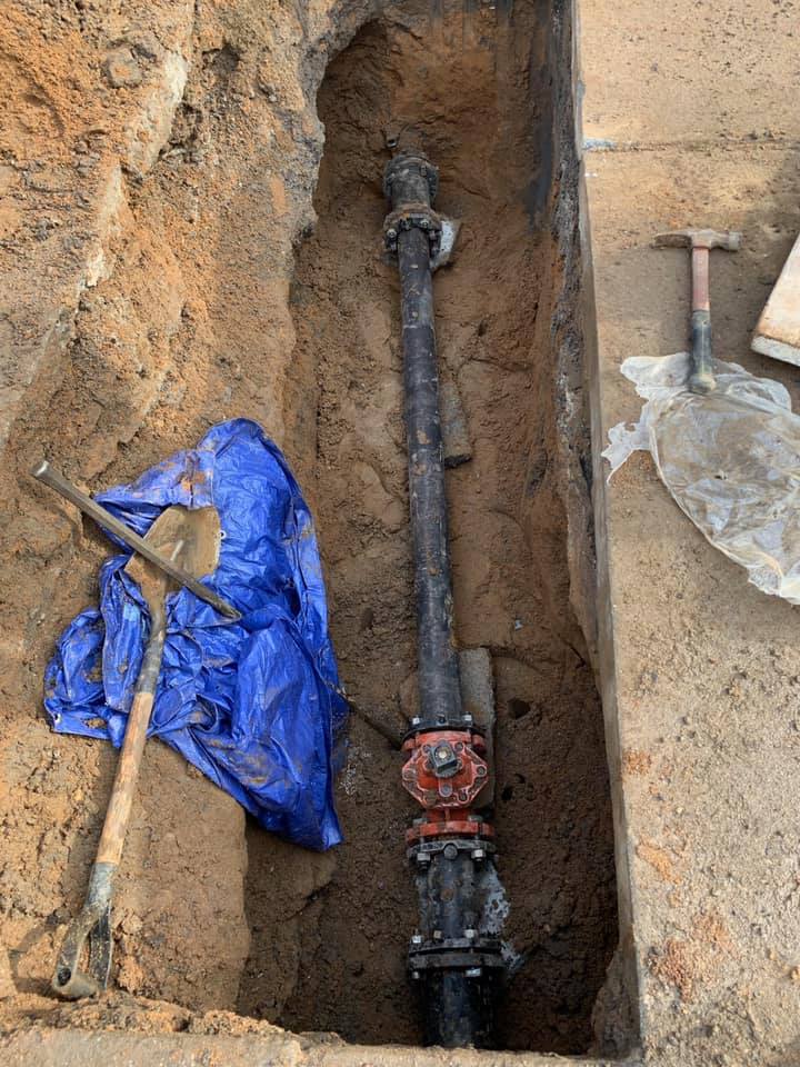 A pipe is laying in the dirt next to a shovel and hammer.