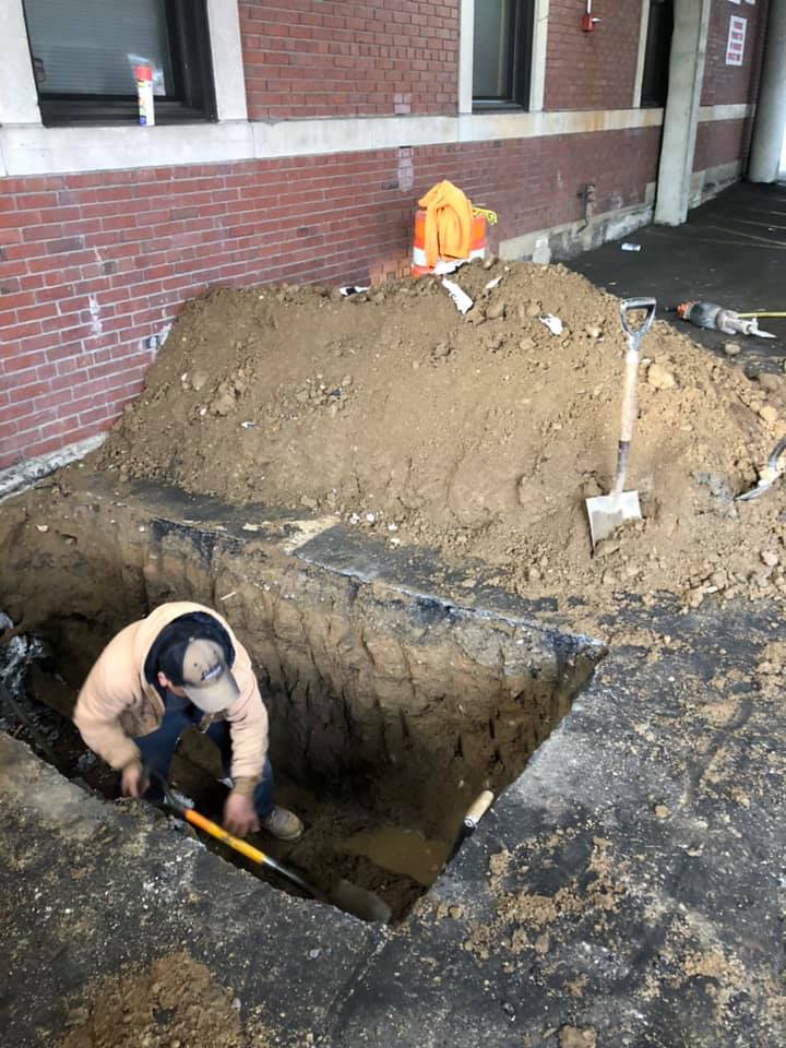 A man is digging a hole in the ground next to a pile of dirt.