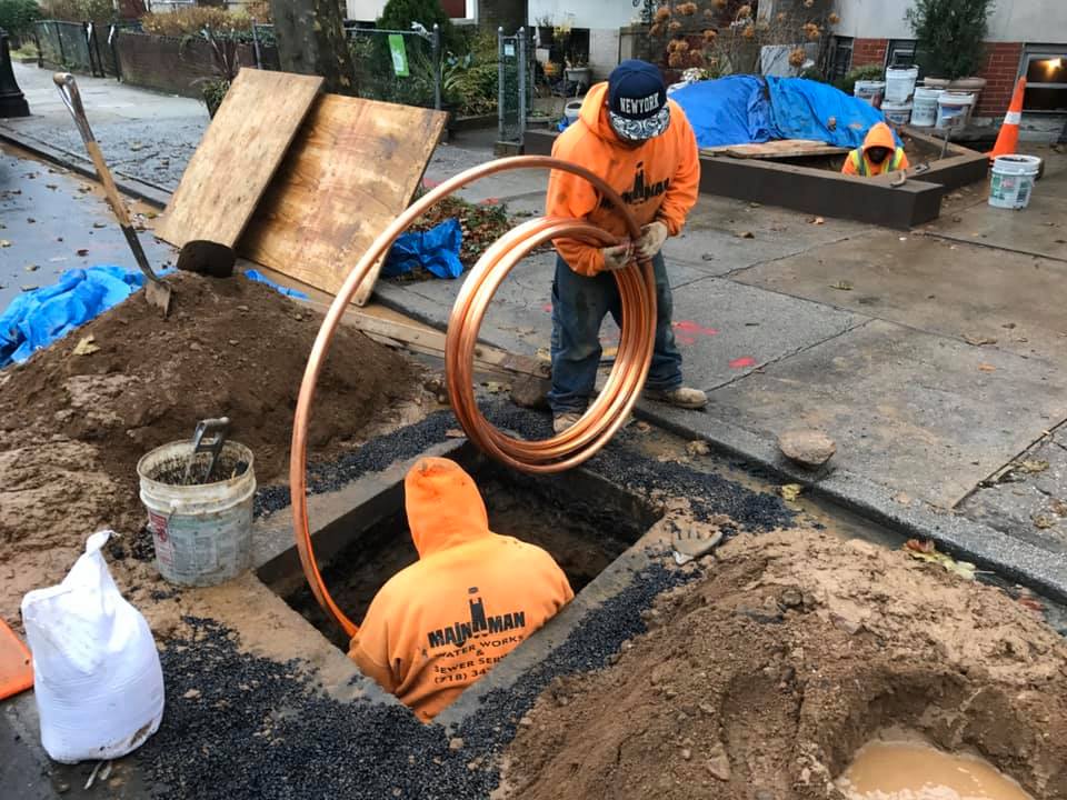 A man is holding a copper pipe in a hole in the ground.