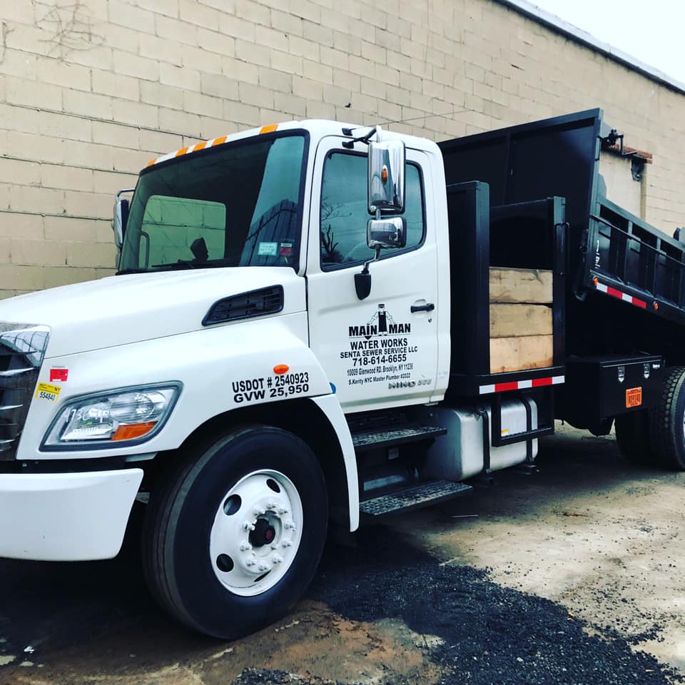 A white dump truck is parked in front of a brick building