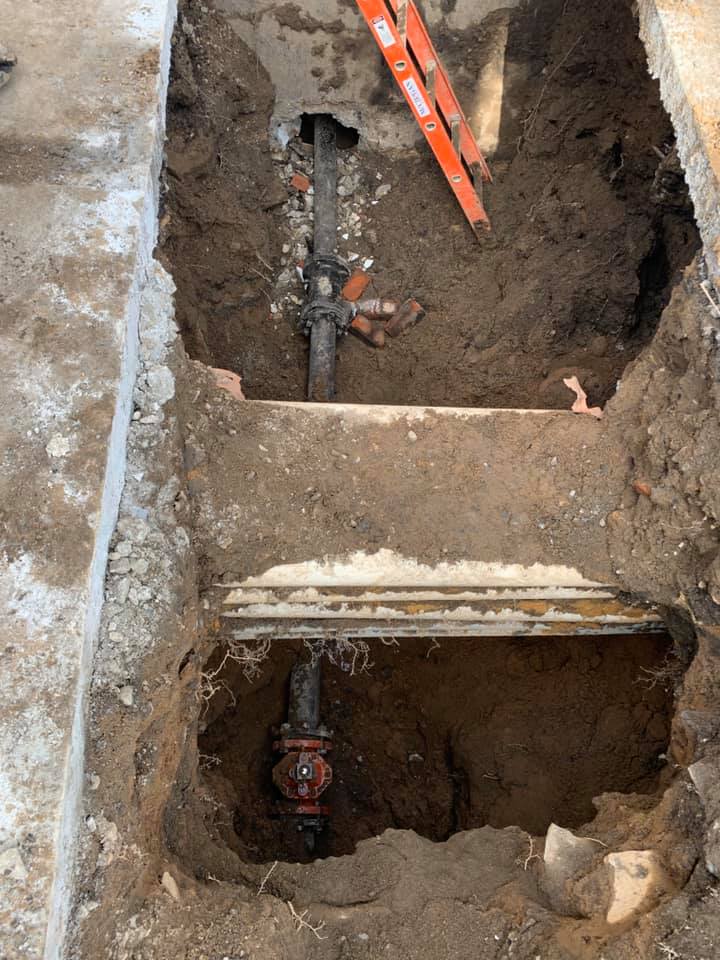 A ladder is sitting in the dirt next to a pipe in the ground.