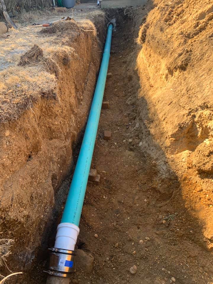 A green pipe is being installed in a trench.
