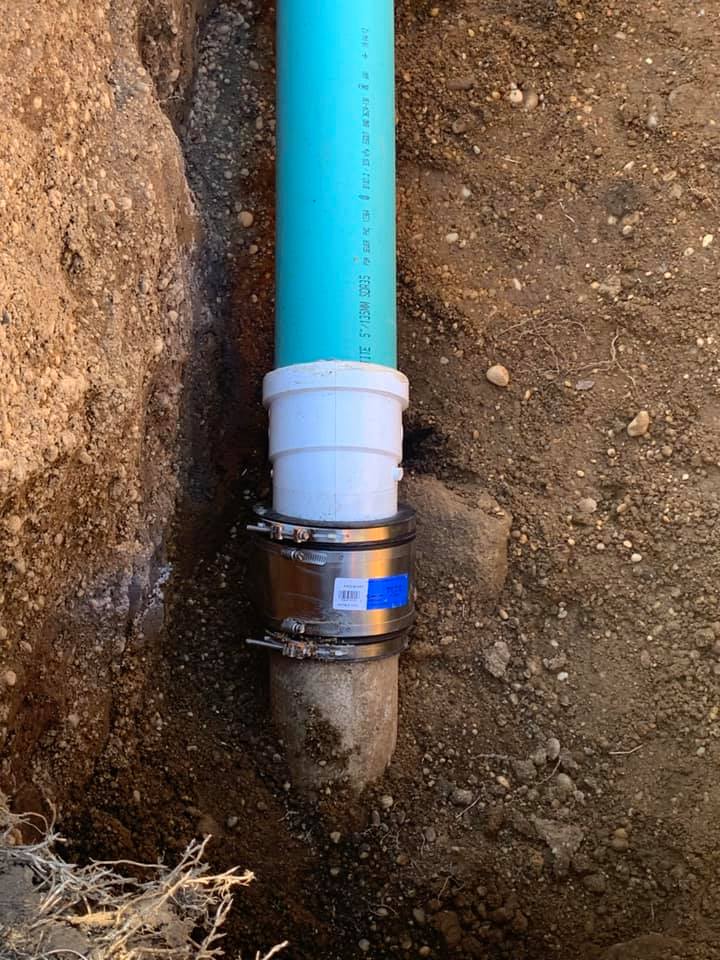 A blue pipe with a white hose attached to it is in the dirt.