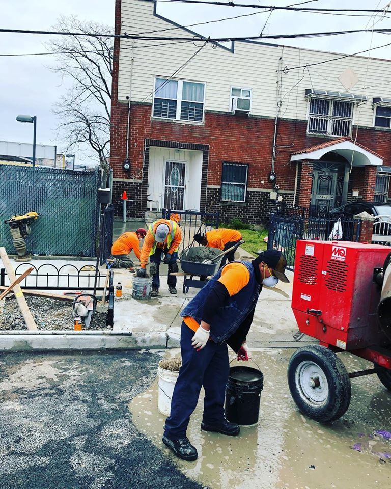 A group of construction workers are working on a sidewalk in front of a building.