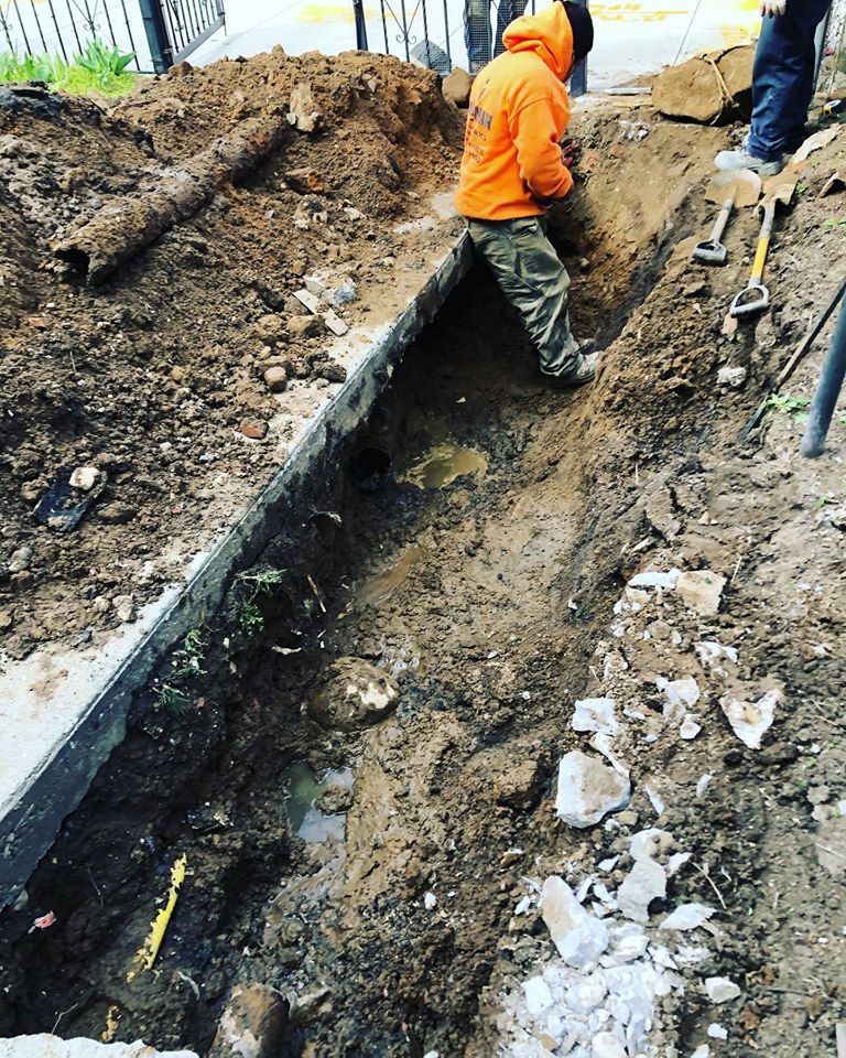 A man in an orange hoodie is digging a trench in the dirt.