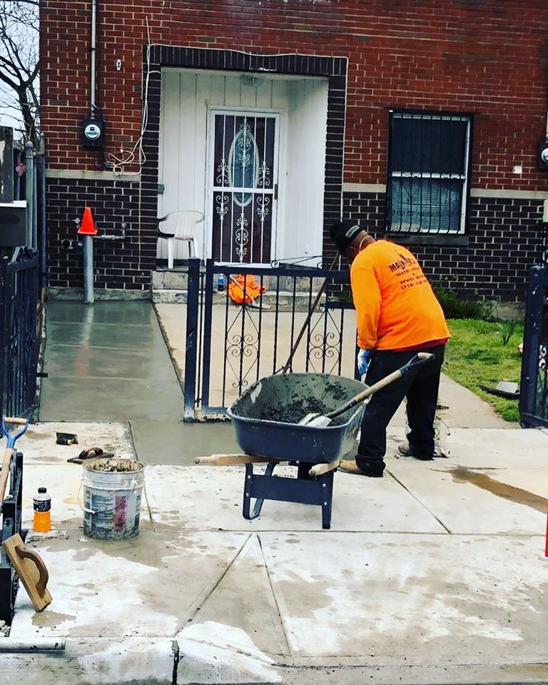 A man in an orange shirt is pushing a wheelbarrow full of cement