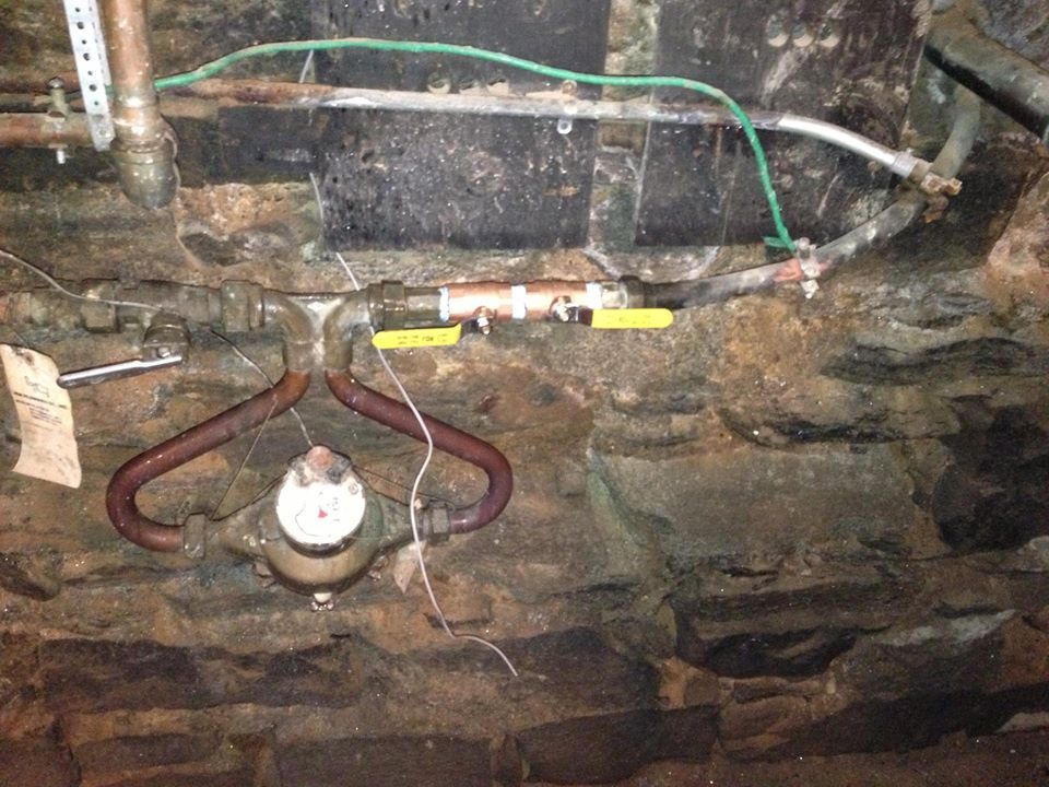 A water meter is attached to a brick wall.