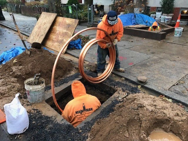 Two men in orange hoodies are working on a copper pipe