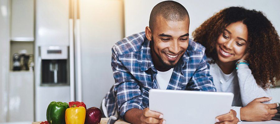 Husband and Wife Holding Tablet in Kitchen and smiling | Four Seasons Sales Property Management Two cups of coffee on table with flowers | Four Seasons Sales Property Management