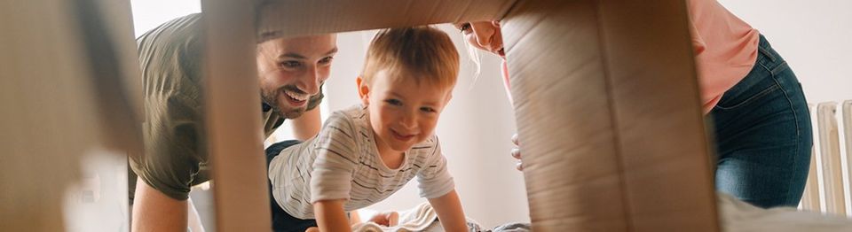 Husband and Wife Holding Tablet in Kitchen and smiling | Four Seasons Sales Property Management Mom, Dad, and Baby playing with cardboard boxes | Four Season Sales Property Management