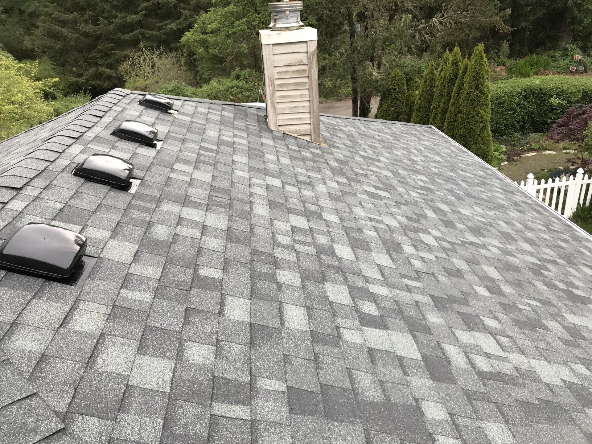 Gray asphalt shingle roof with four skylights and a chimney.
