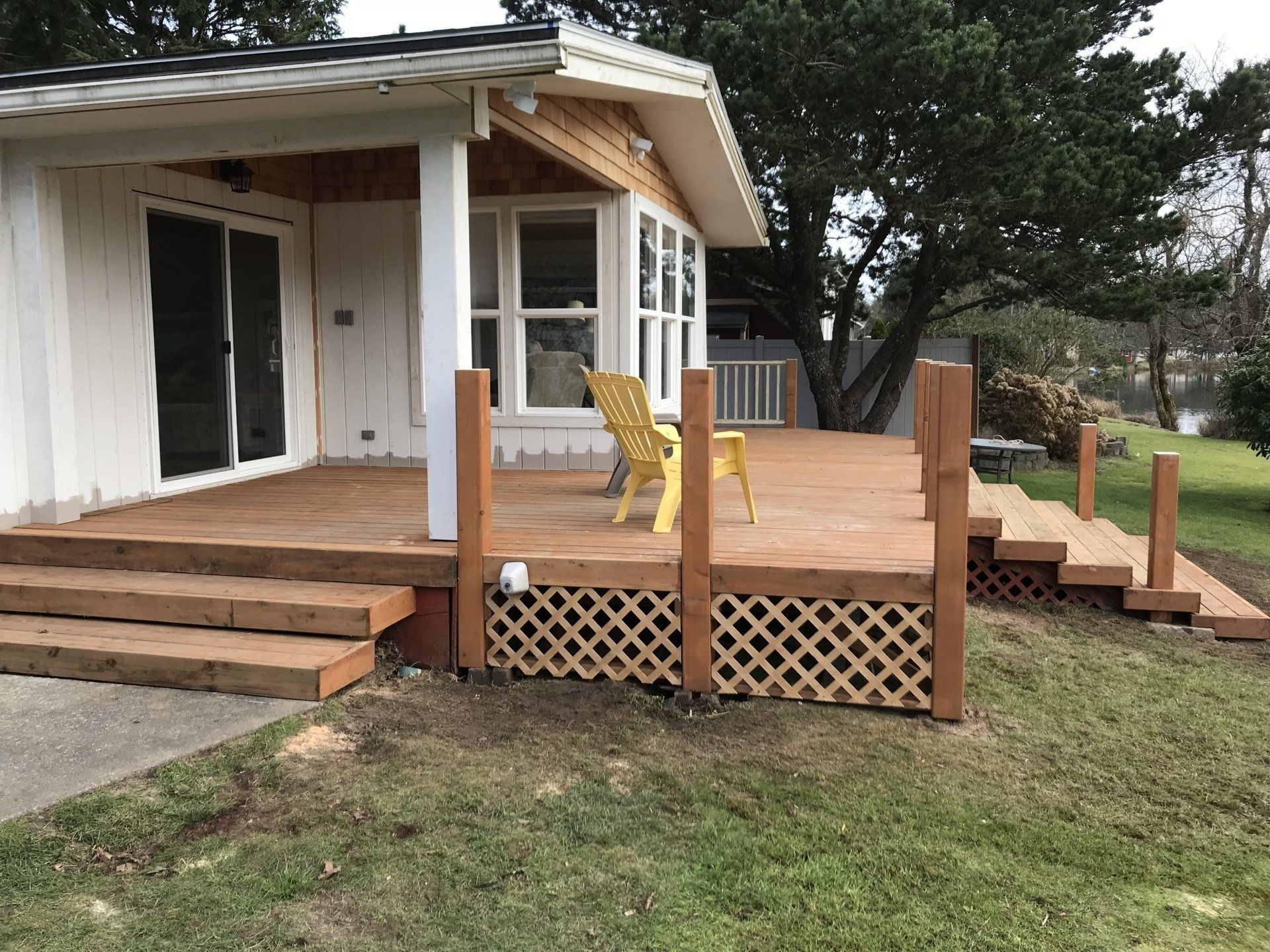 Wooden deck with steps, lattice detailing, and a yellow chair, connected to a white house with sliding doors.