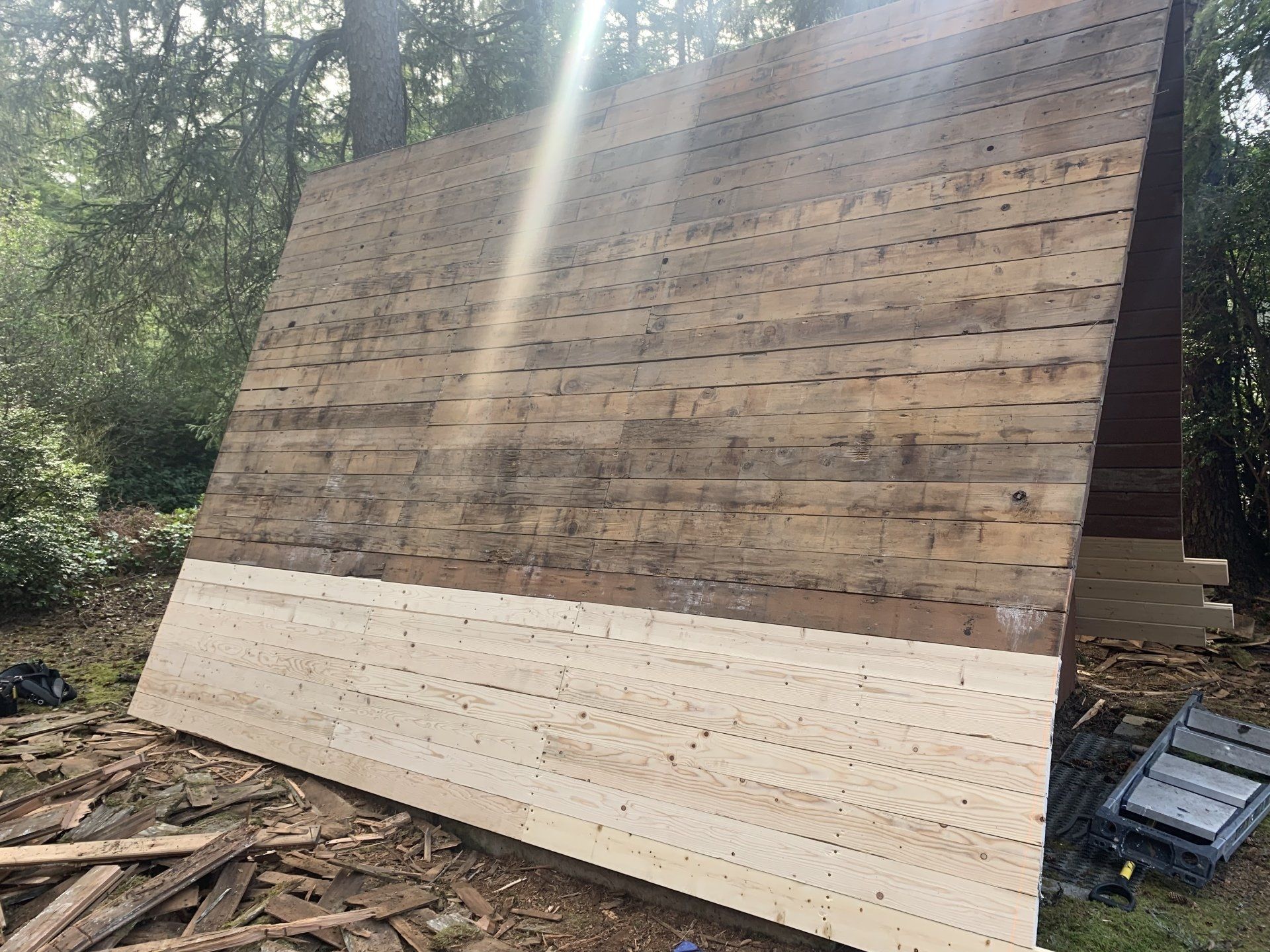 Wooden A-frame structure being renovated; light-colored wood installed on the lower half, old weathered wood on the upper.