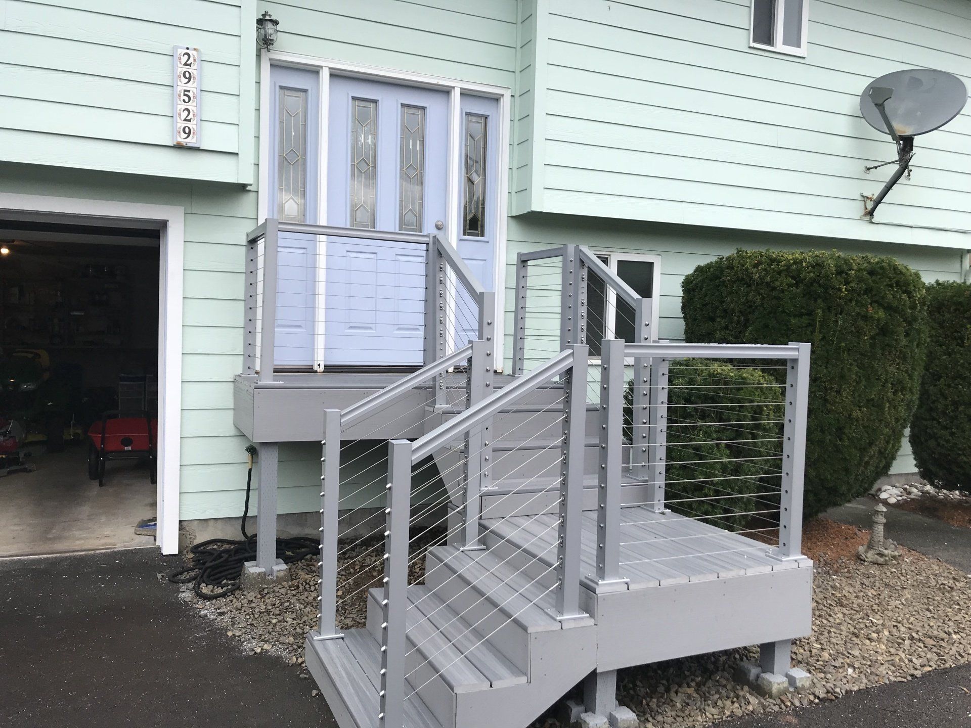 Gray wooden porch with stairs and cable railing, leading to a light blue front door.