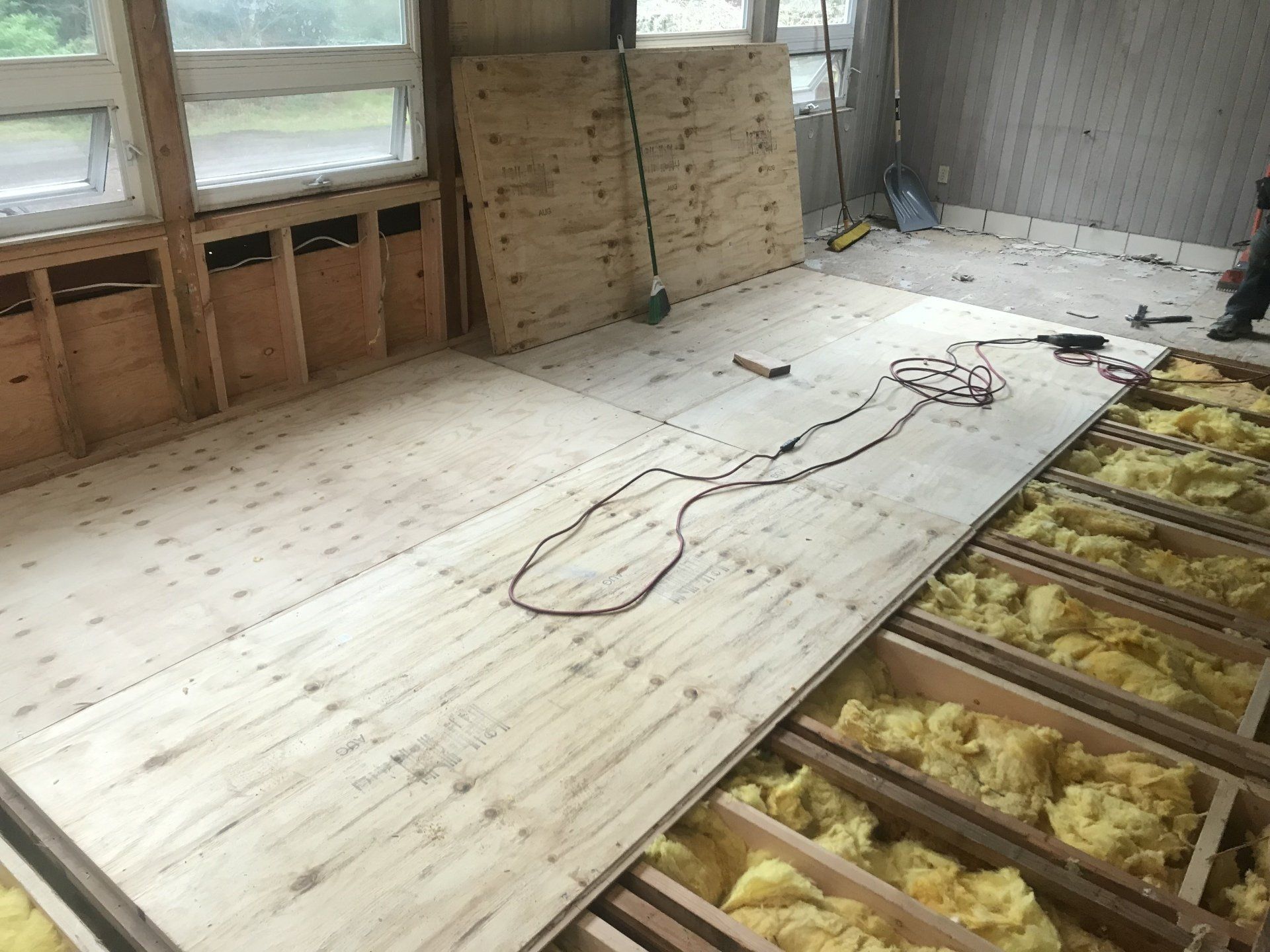 Construction site, installing plywood subfloor over joists, insulation visible.