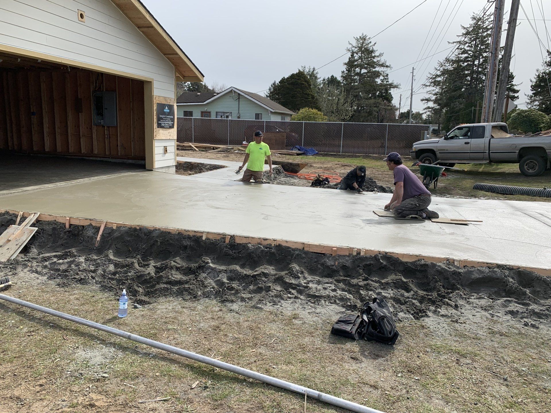 Workers smoothing wet concrete for a driveway in front of a garage.