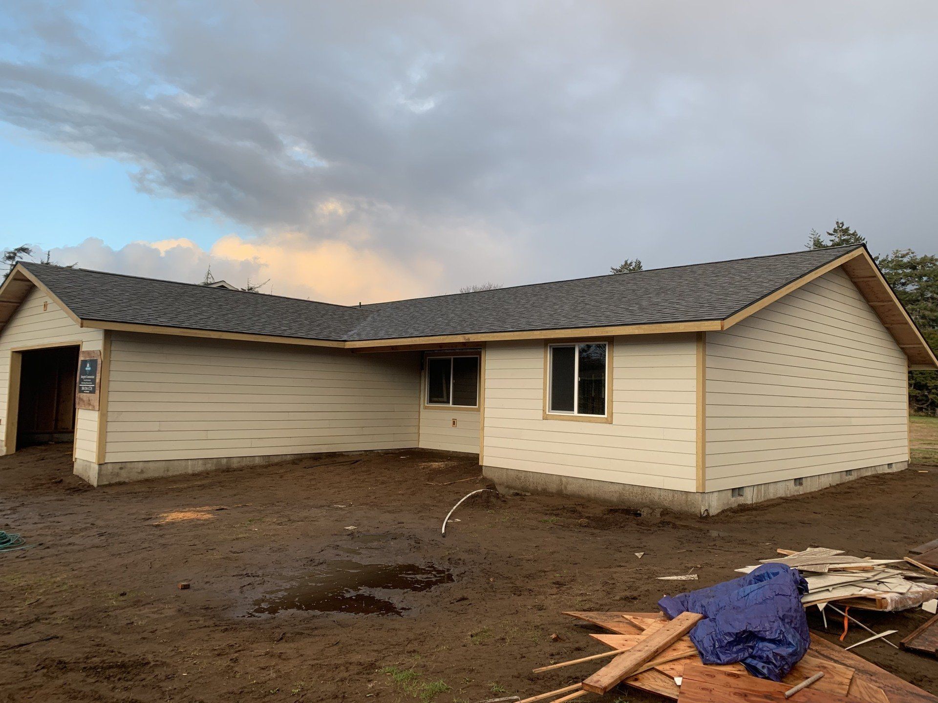 Tan house under construction with gray roof and cloudy sky.