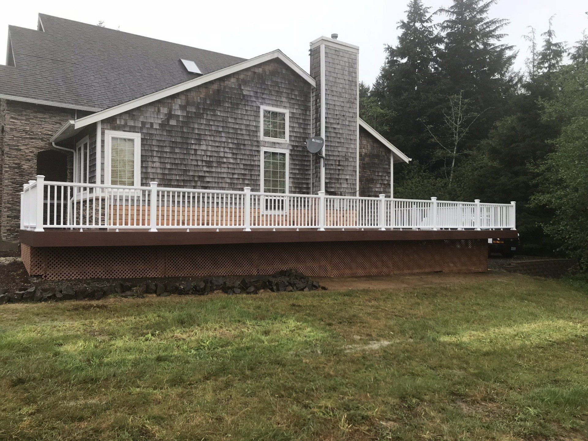 Backyard deck on a weathered house. White railing, brown deck, and a tall chimney. Green grass in the foreground.