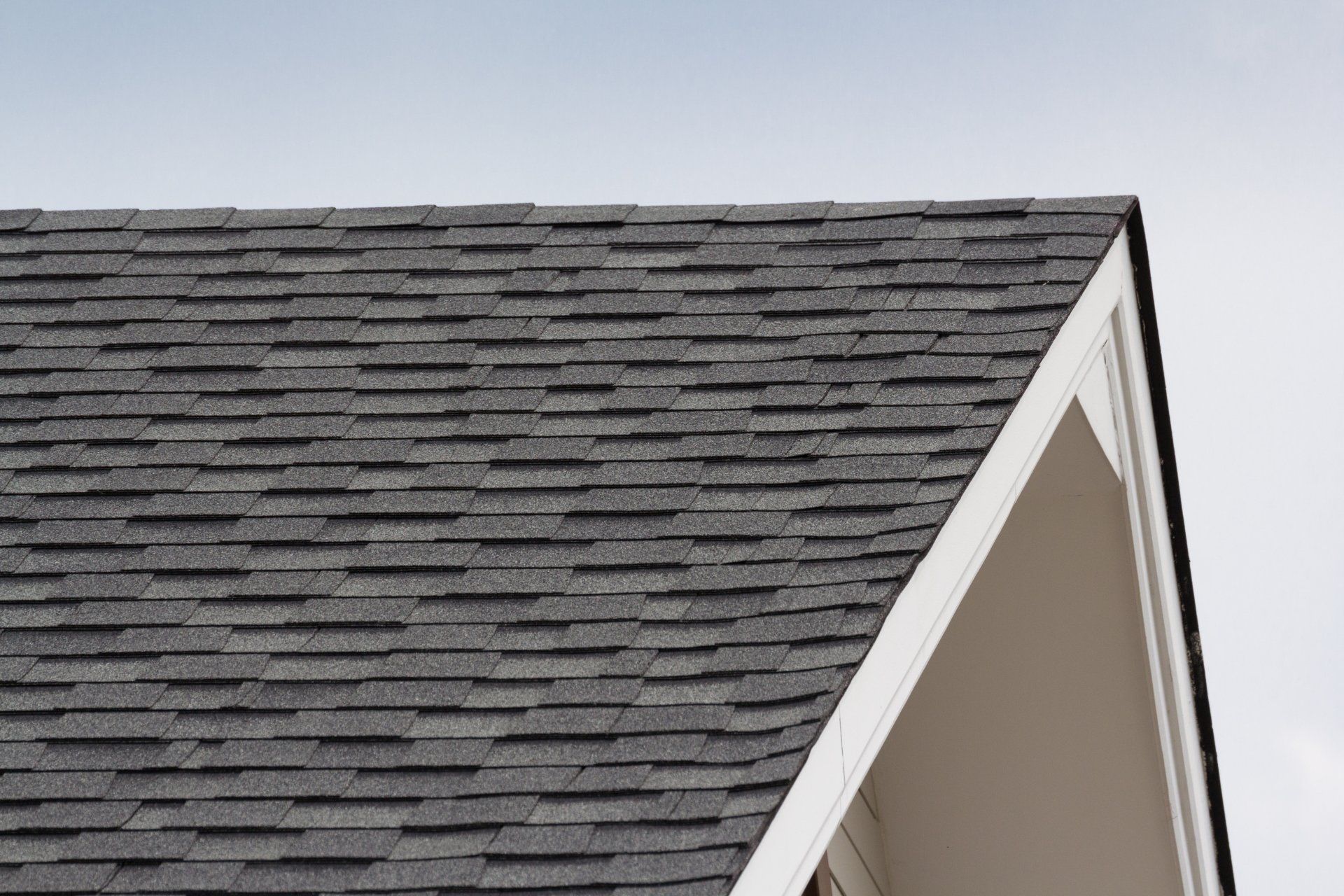 Gray asphalt shingle roof on a white house, against a light blue sky.