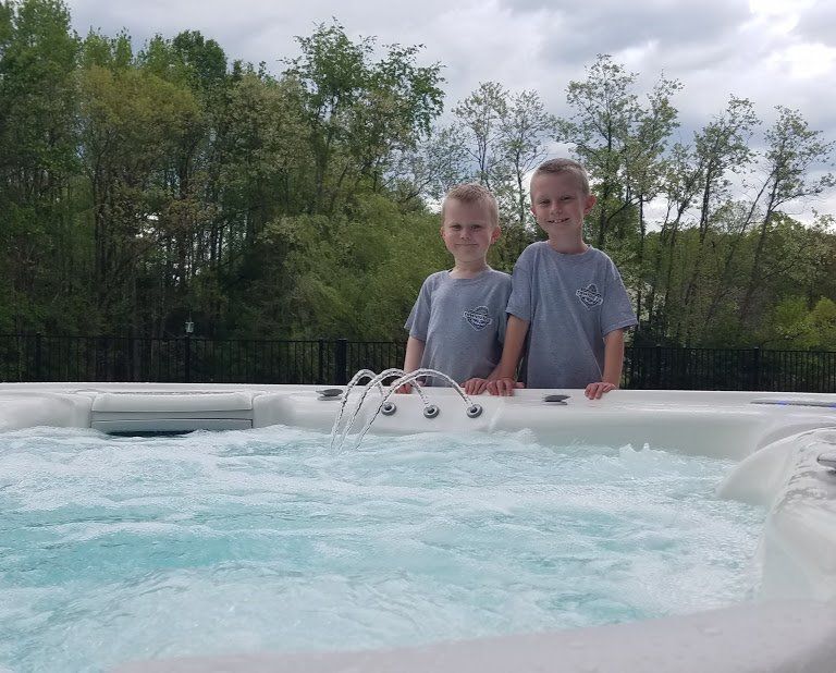 Two young boys are standing on the edge of a hot tub
