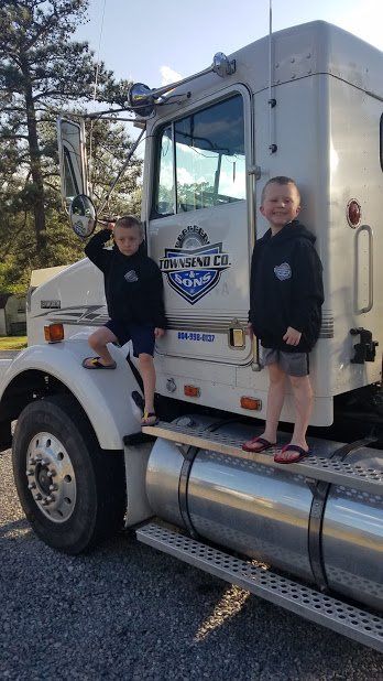 Two young boys are standing on the back of a semi truck.