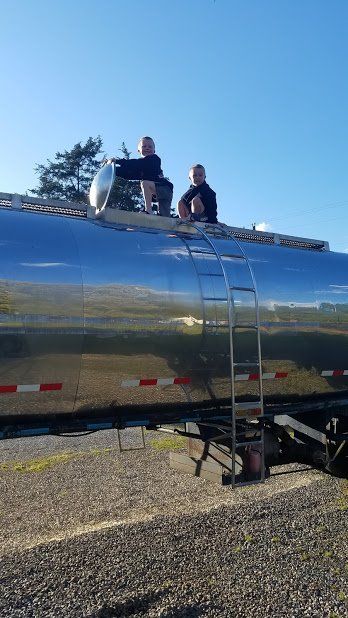 Two men are sitting on top of a large tanker truck.
