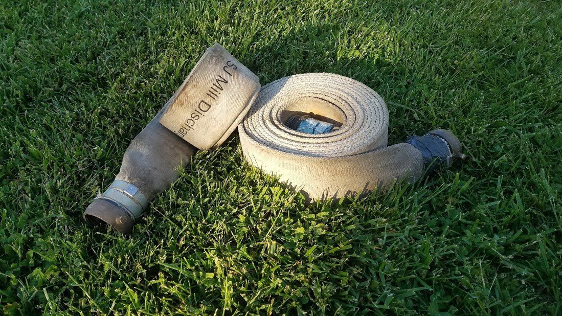 A fire hose is laying on top of a lush green field.