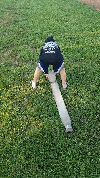 A person is bending over in the grass with a hose.
