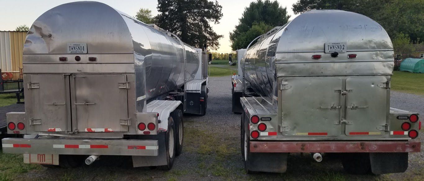 Two tanker trucks are parked next to each other on a gravel road.