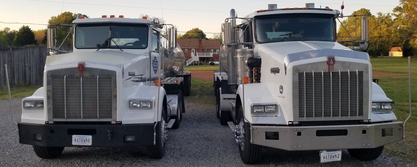 Two semi trucks are parked next to each other on a gravel road.