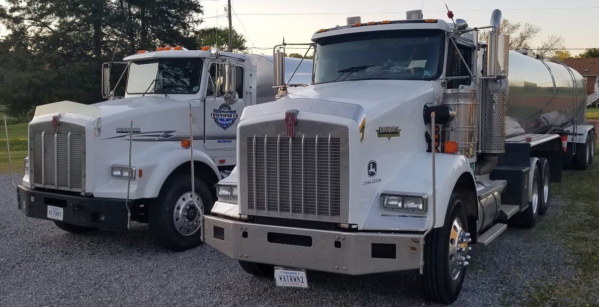 Two semi trucks are parked next to each other on a gravel road.