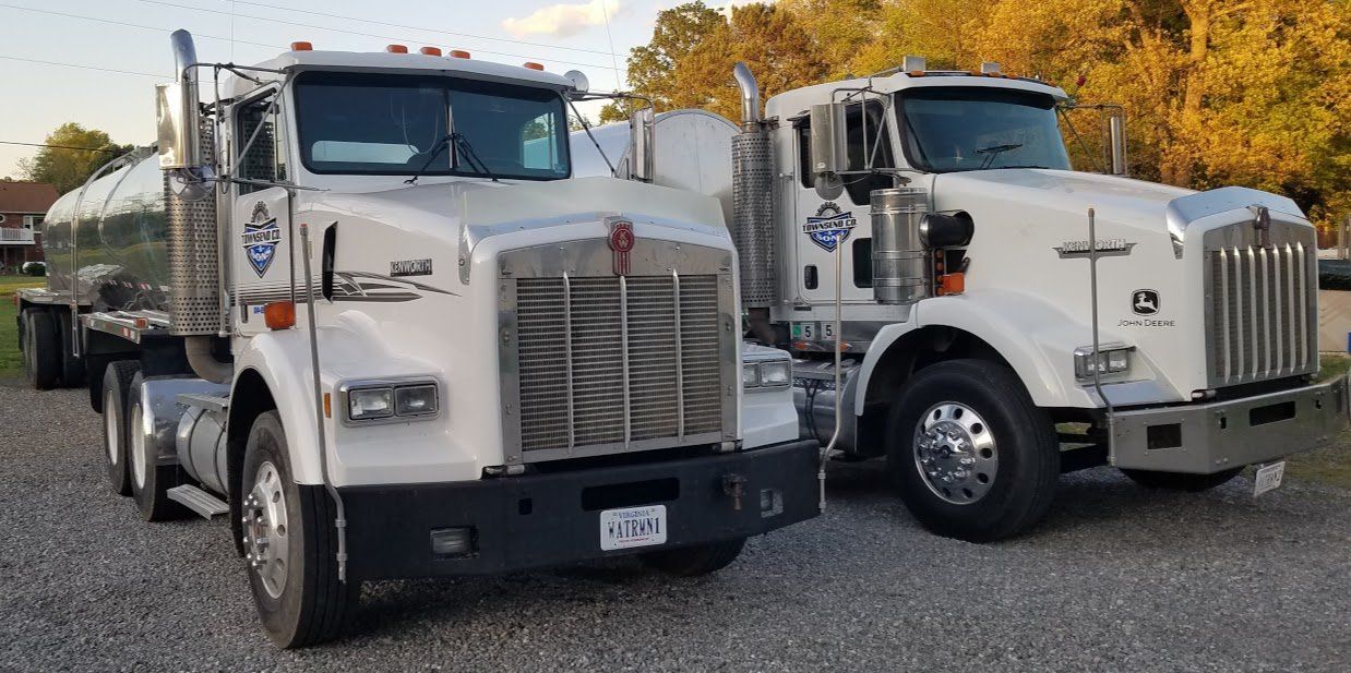 Two semi trucks are parked next to each other on a gravel road.